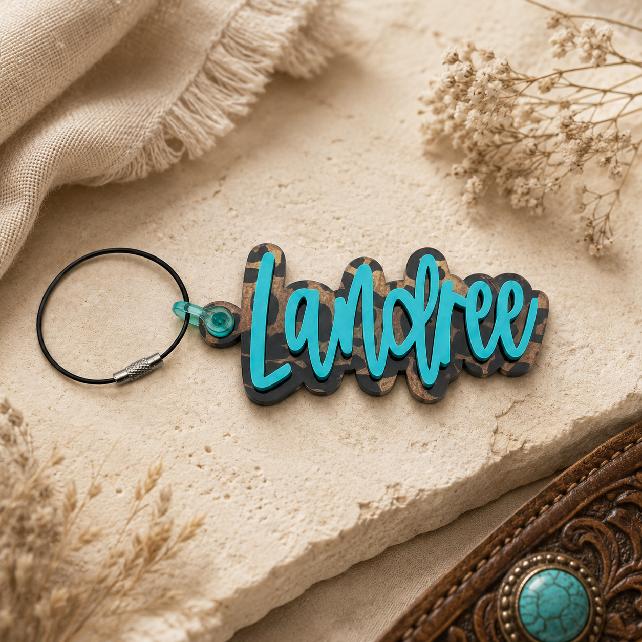 Keychain with 'Landfee' text on a textured surface with dried flowers and fabric.