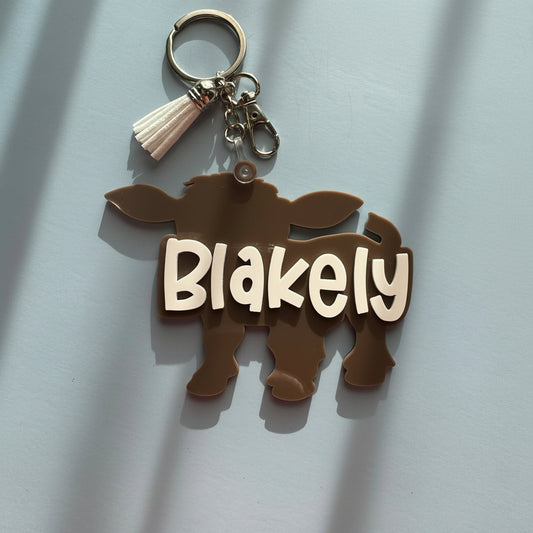 Keychain with cow design and 'Blakely' text on a light blue background