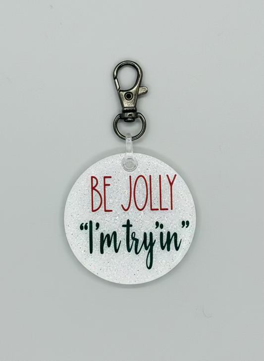 2" round keychain. White Glitter backer with Be Jolly in red text and "I'm Try'in" in green text