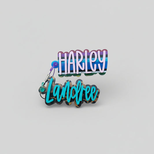 Hand holding a colorful keychain with 'HARLEY Landree' text against a stone wall background